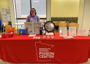 Staff member at a Minnesota Regional Poison Center outreach table with educational materials and poison prevention resources.